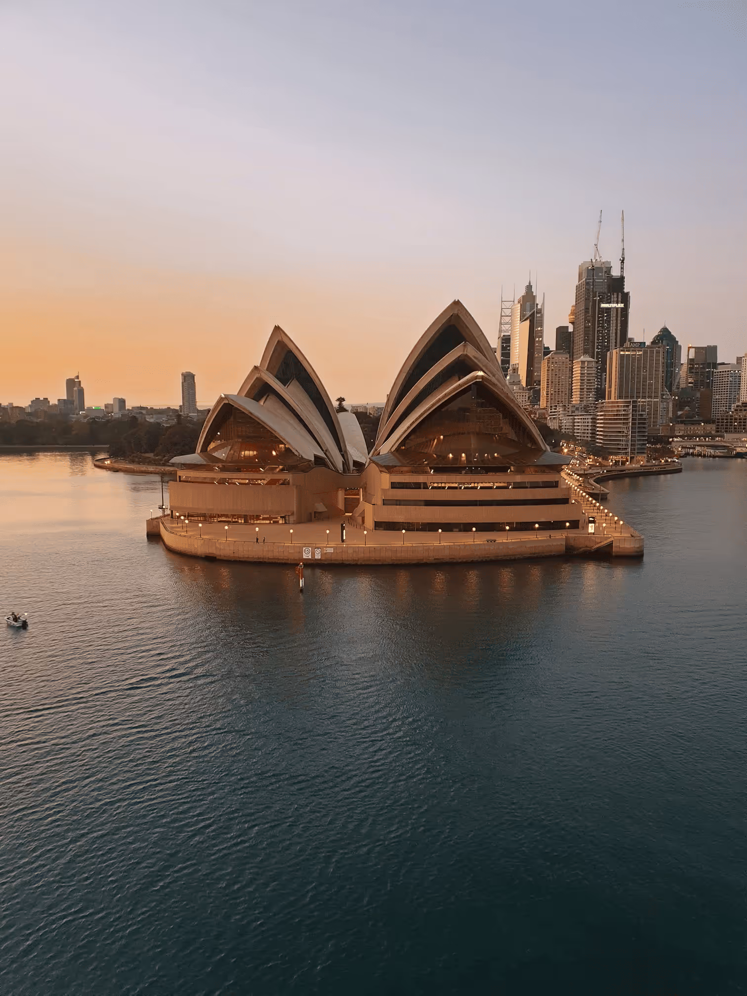 Sydney Opera House with city skyline at sunset and calm harbor water.