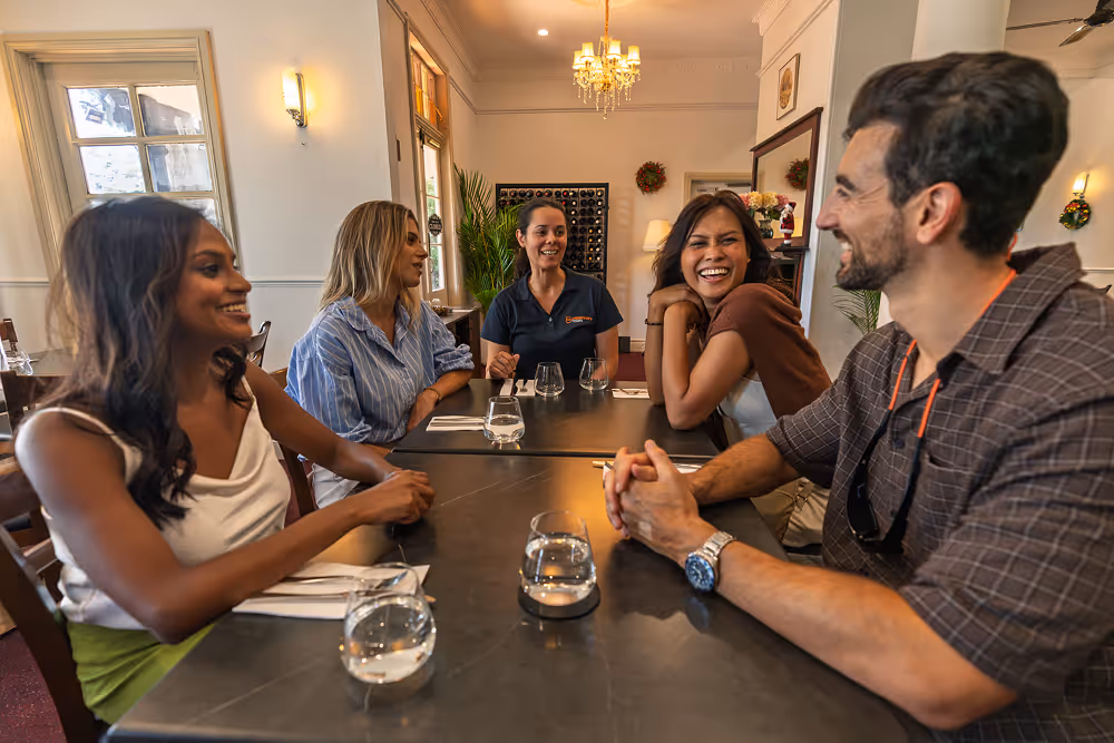 Five people sitting around a table in a restaurant, smiling and engaged in conversation with glasses of water on the table.