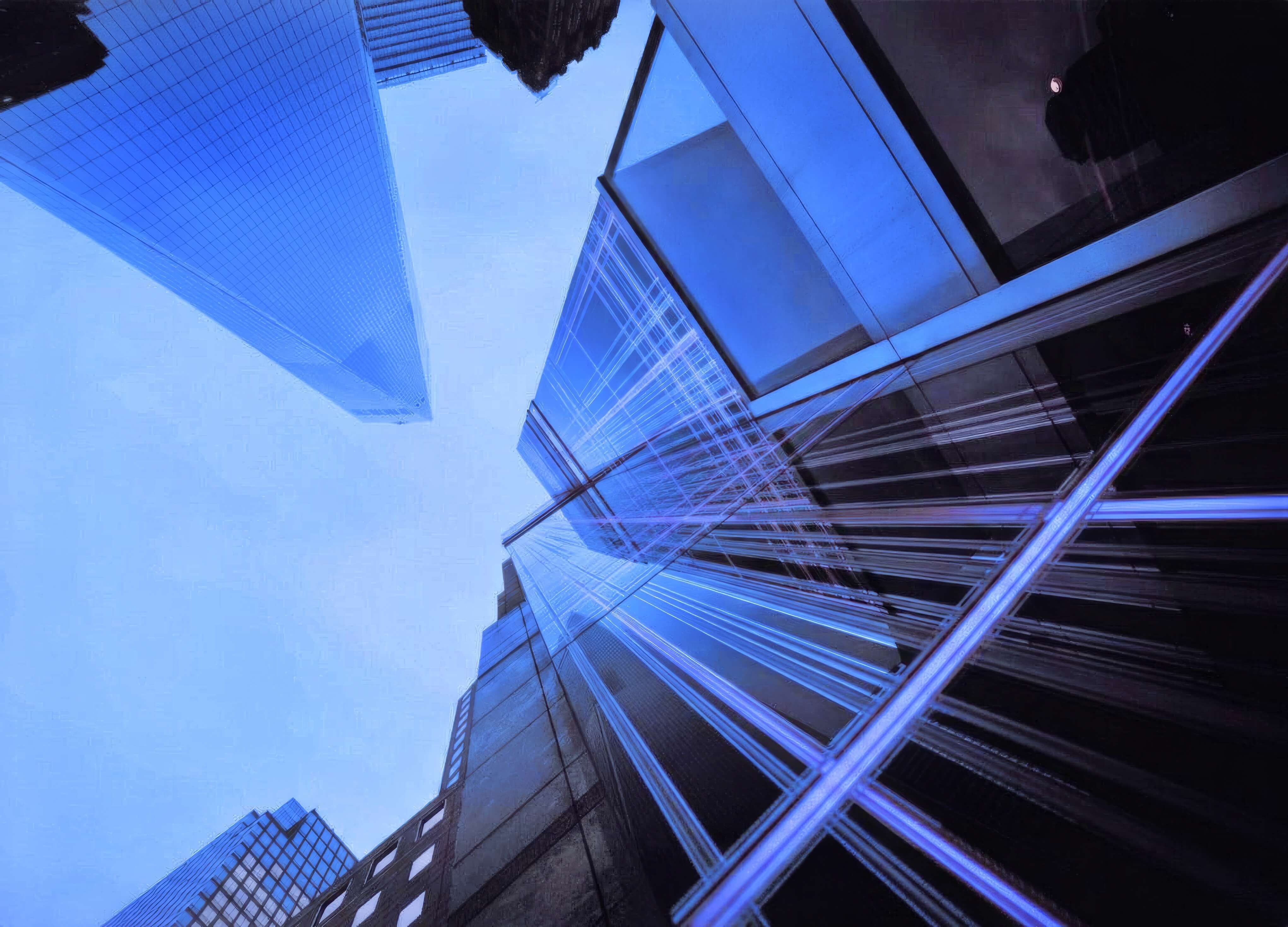 Upward view of modern skyscrapers with glass facades reflecting blue sky and intersecting lines of light on the closest building.