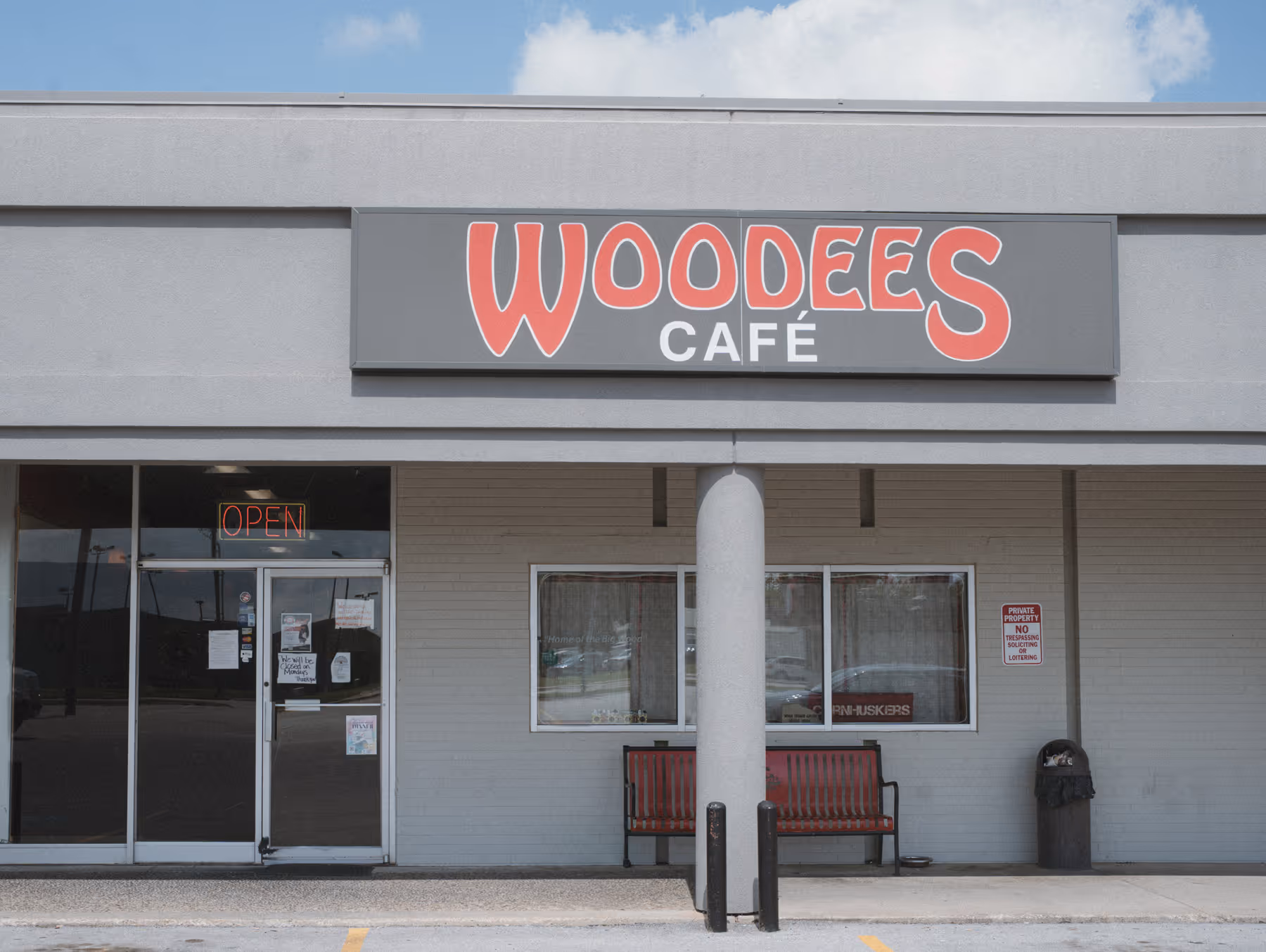 Exterior of Woodees Café with a red open sign and a red bench outside under a blue sky.