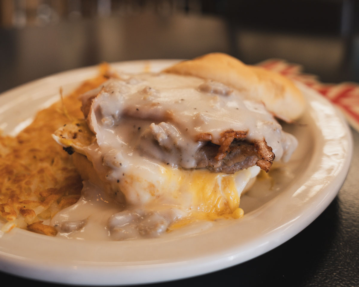 Breakfast plate with sausage gravy over eggs and hash browns beside a biscuit.