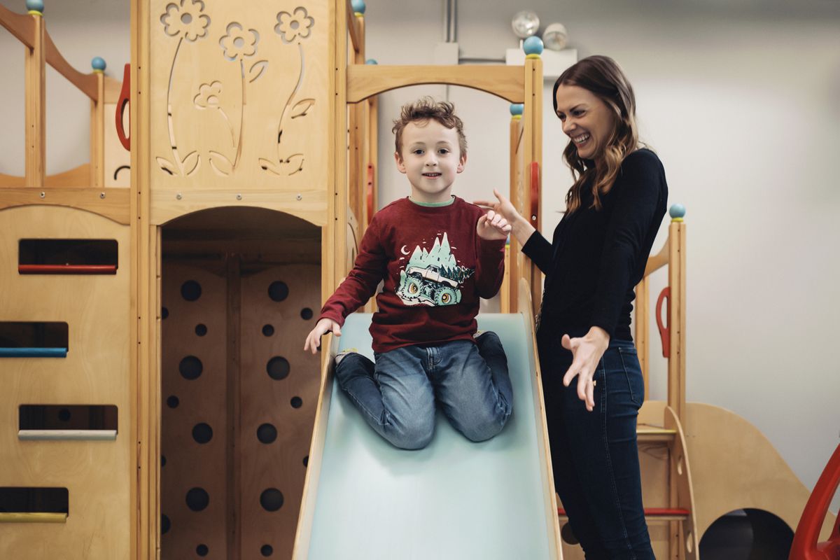 Meaghan Milbourn smiling and playing with a young boy sliding down the slide