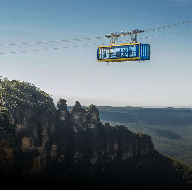 Cable car with passengers traveling over a forested mountain cliff with a clear sky background.