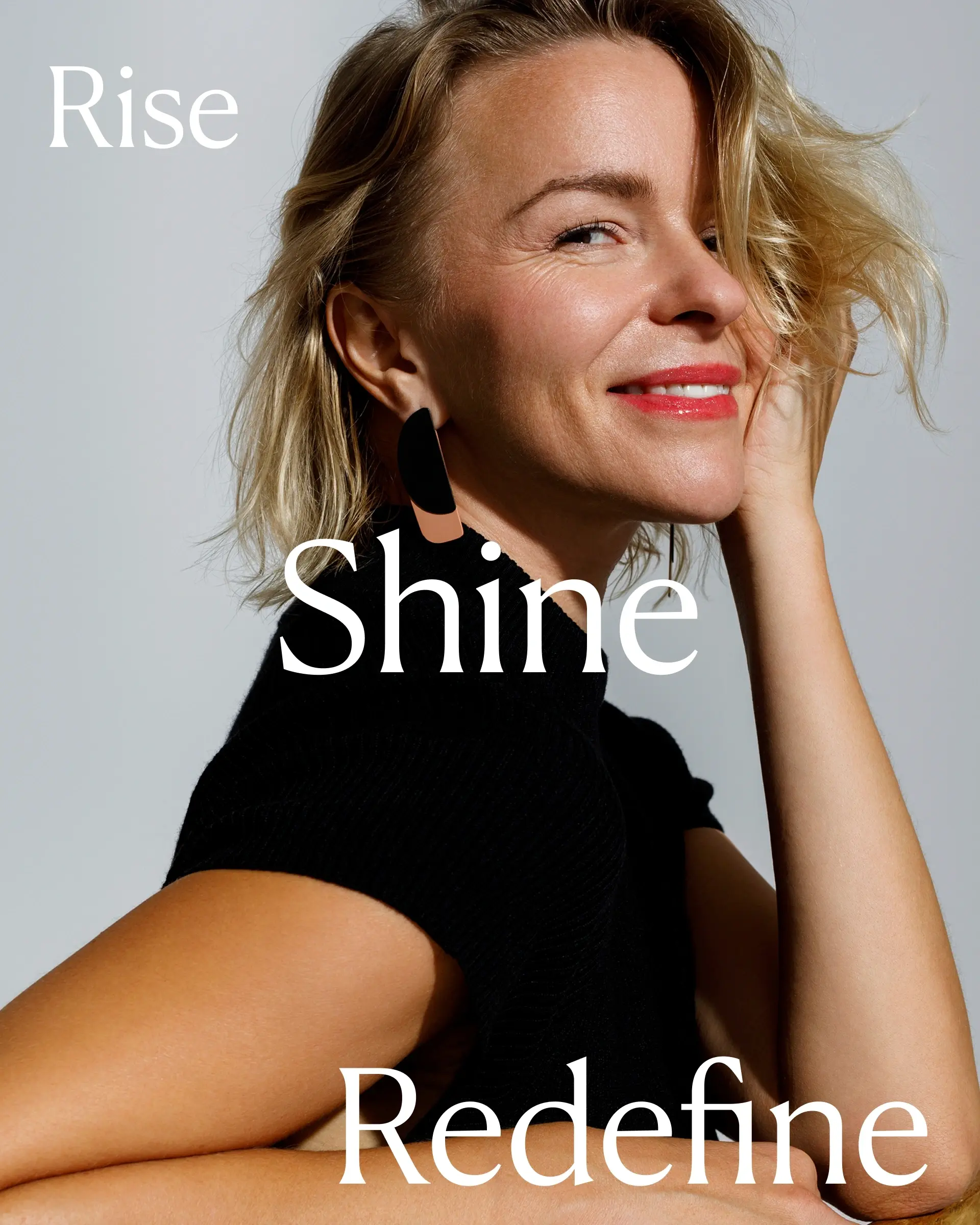Smiling blonde woman with red lipstick and black top posing against a plain background with the words Rise, Shine, Redefine.