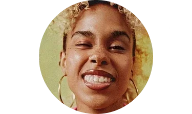 Close-up of a young woman with curly hair, smiling with one eye closed and wearing large hoop earrings.