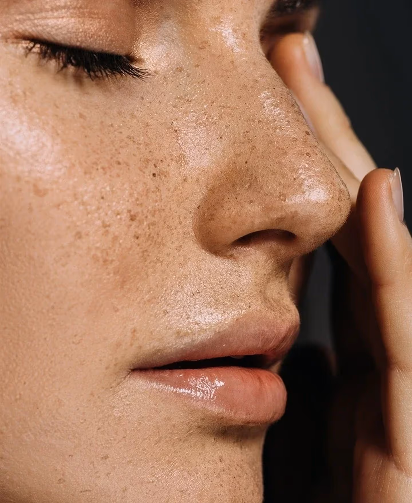 Close-up of a freckled face with closed eyes and fingers gently touching the forehead.
