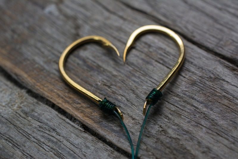 Two fish hooks symmetrically placed in the shape of a heart, representing a romantic getaway in Alaska.