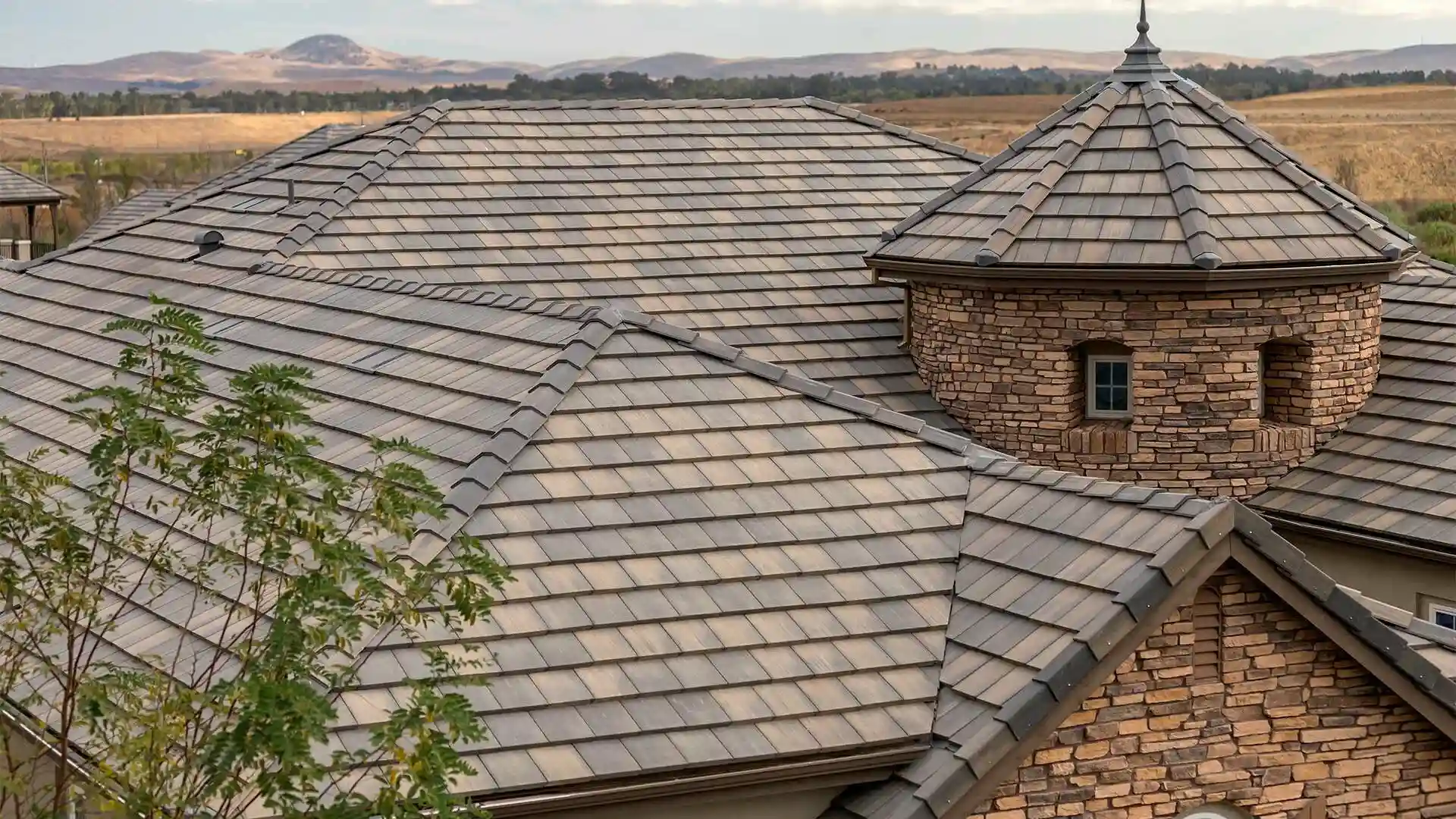 Roof with gray tiles and a stone turret with small windows against a rural landscape background.