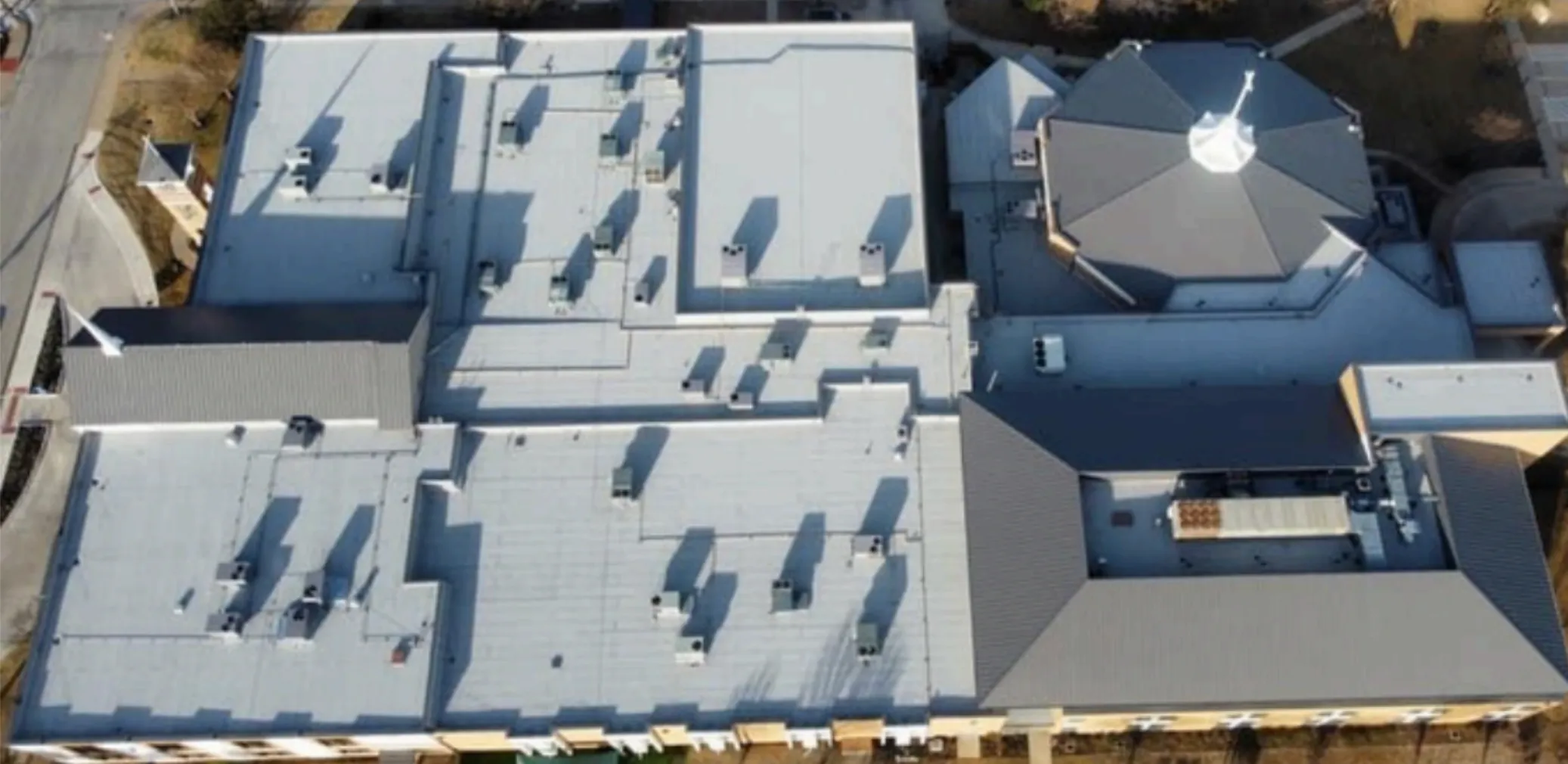 Aerial view of a large building complex with multiple flat and pitched roofs, including a distinctive octagonal section with a white cupola.