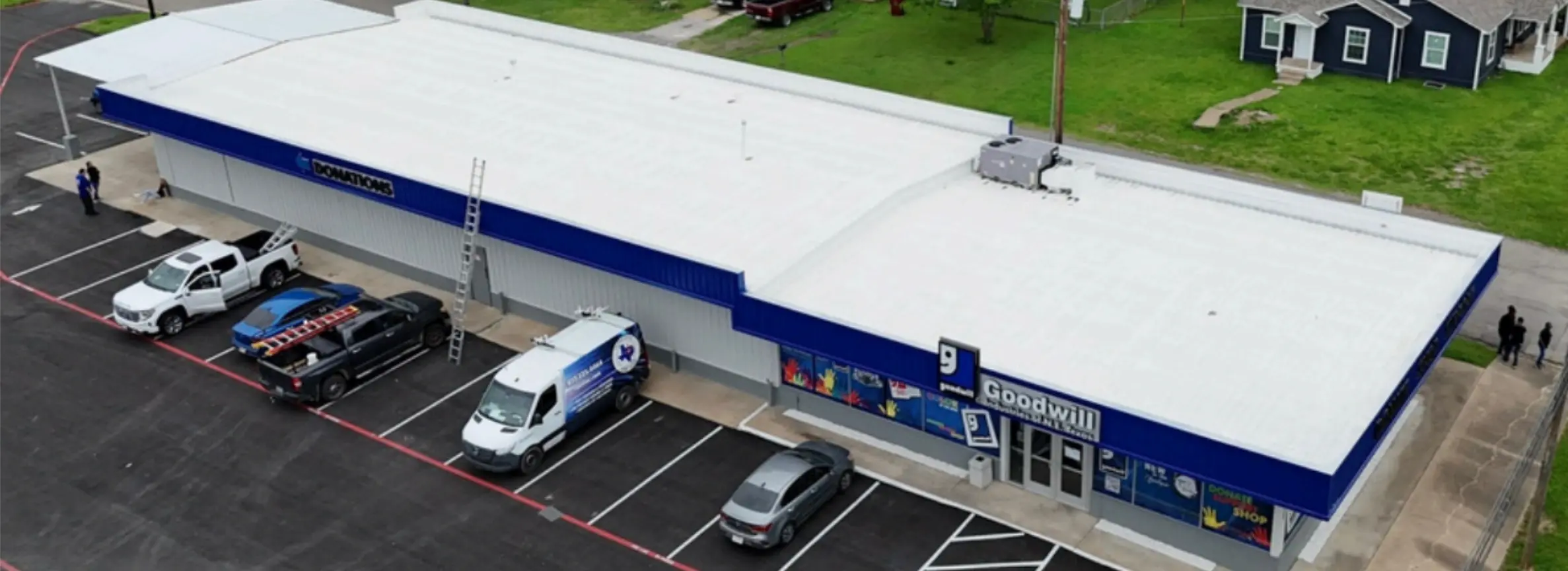 Aerial view of a Goodwill store with a white roof, blue signage, and several vehicles parked in front.