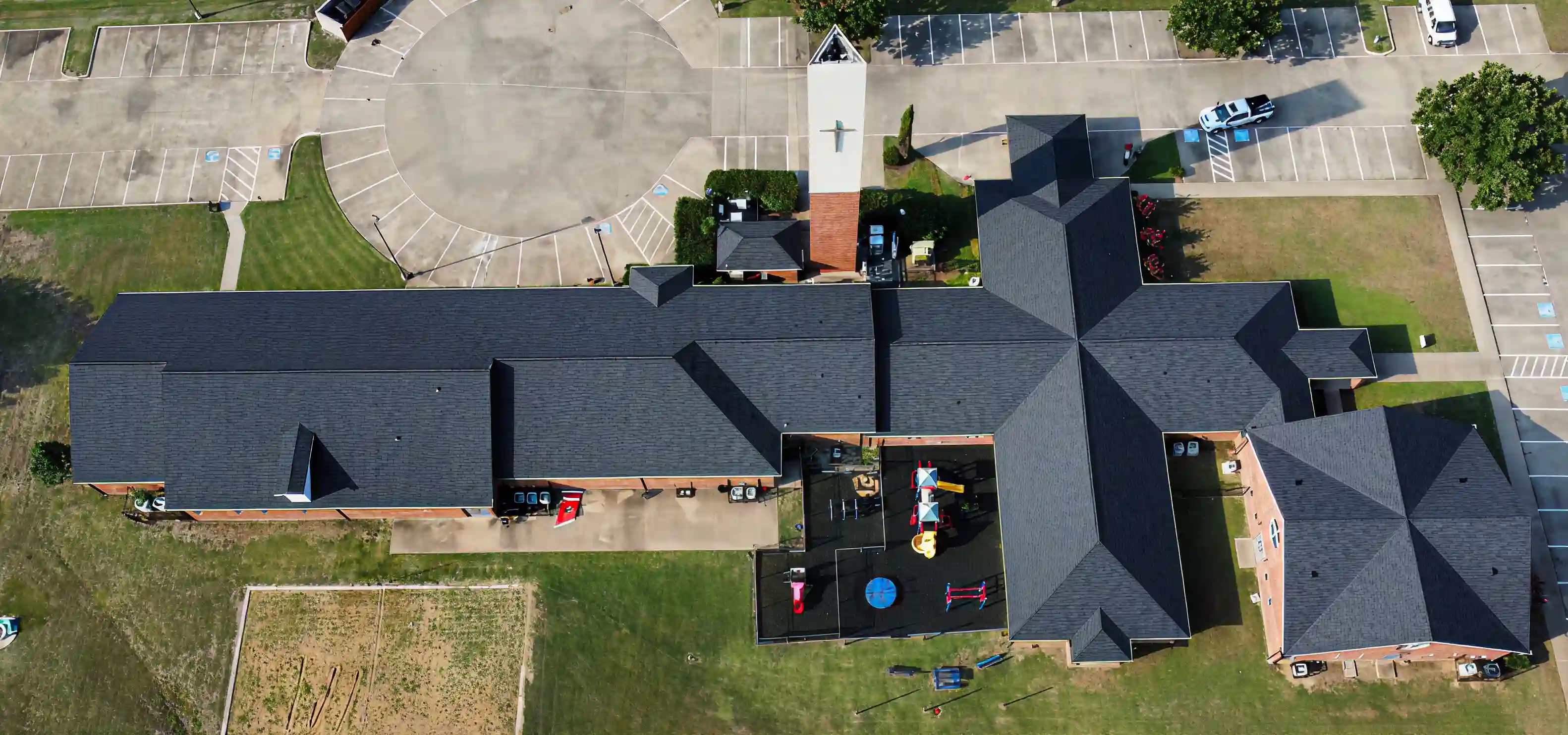 Aerial view of a large building complex with a playground, parking lots, and surrounding grass areas.
