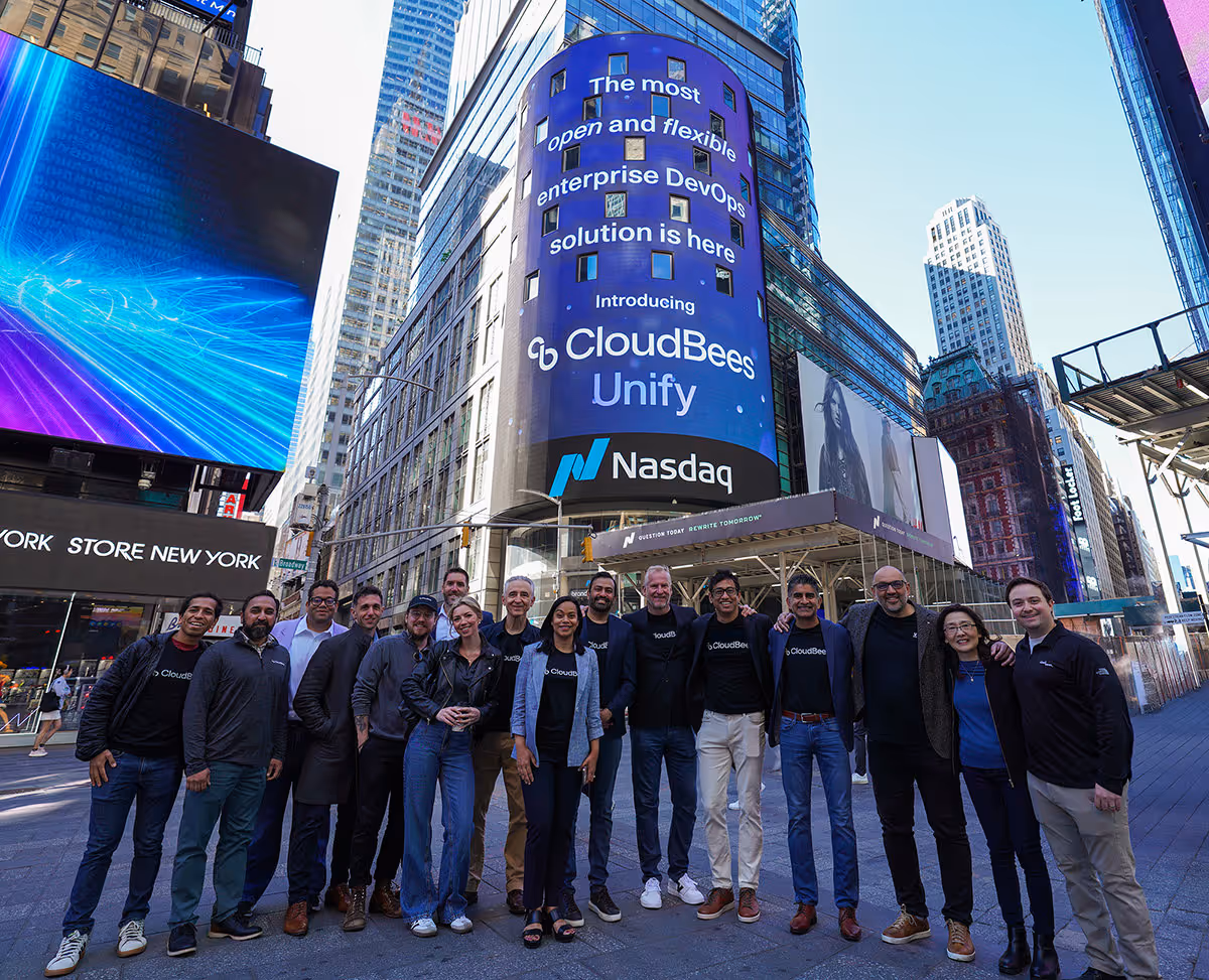 Group of people posing in front of a tall digital billboard in Times Square displaying CloudBees Unify and Nasdaq branding.
