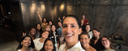 Group of diverse smiling founders in Dubai taking a selfie in a dimly lit room with exposed concrete walls.