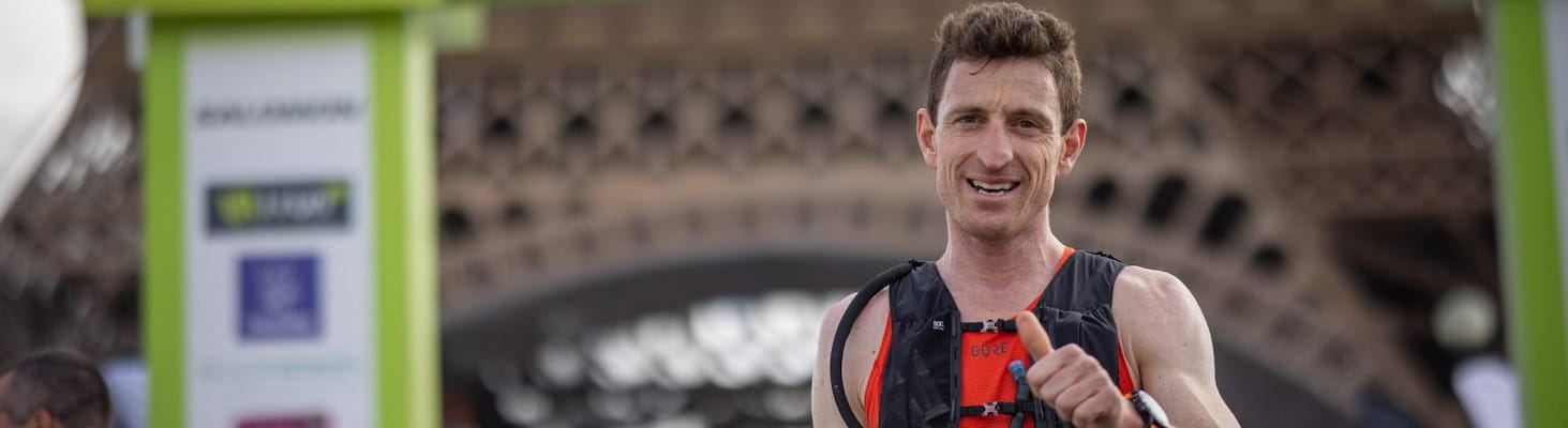 Un coureur souriant franchit la ligne d’arrivée de l’EcoTrail Paris, avec la tour Eiffel en arrière-plan.
