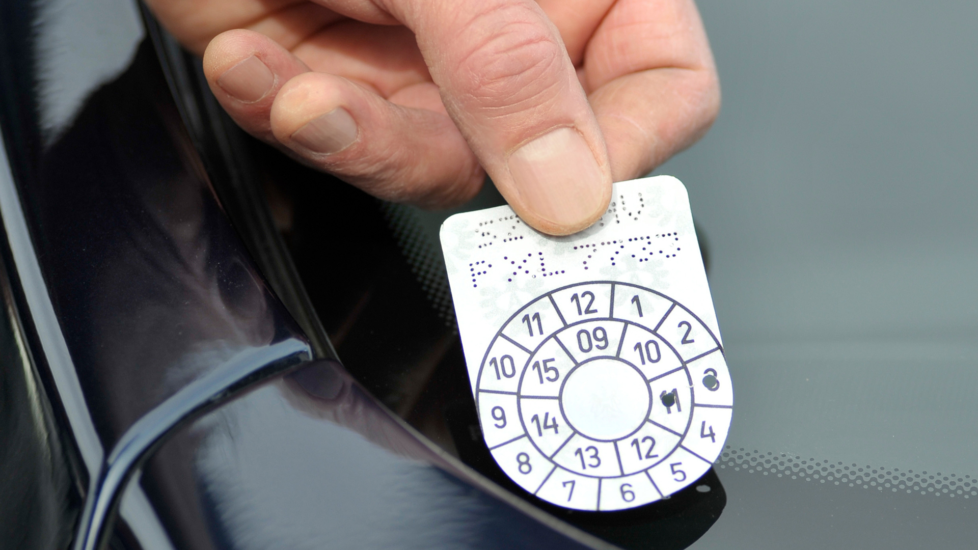 Hand holding a circular vehicle inspection sticker against a car windshield.