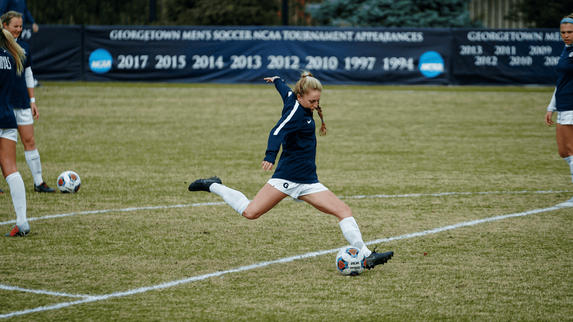 Joueuse de football en bleu marine et blanc tapant un ballon sur le terrain.