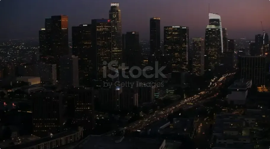 Nighttime cityscape with illuminated skyscrapers and busy traffic along a lit highway.