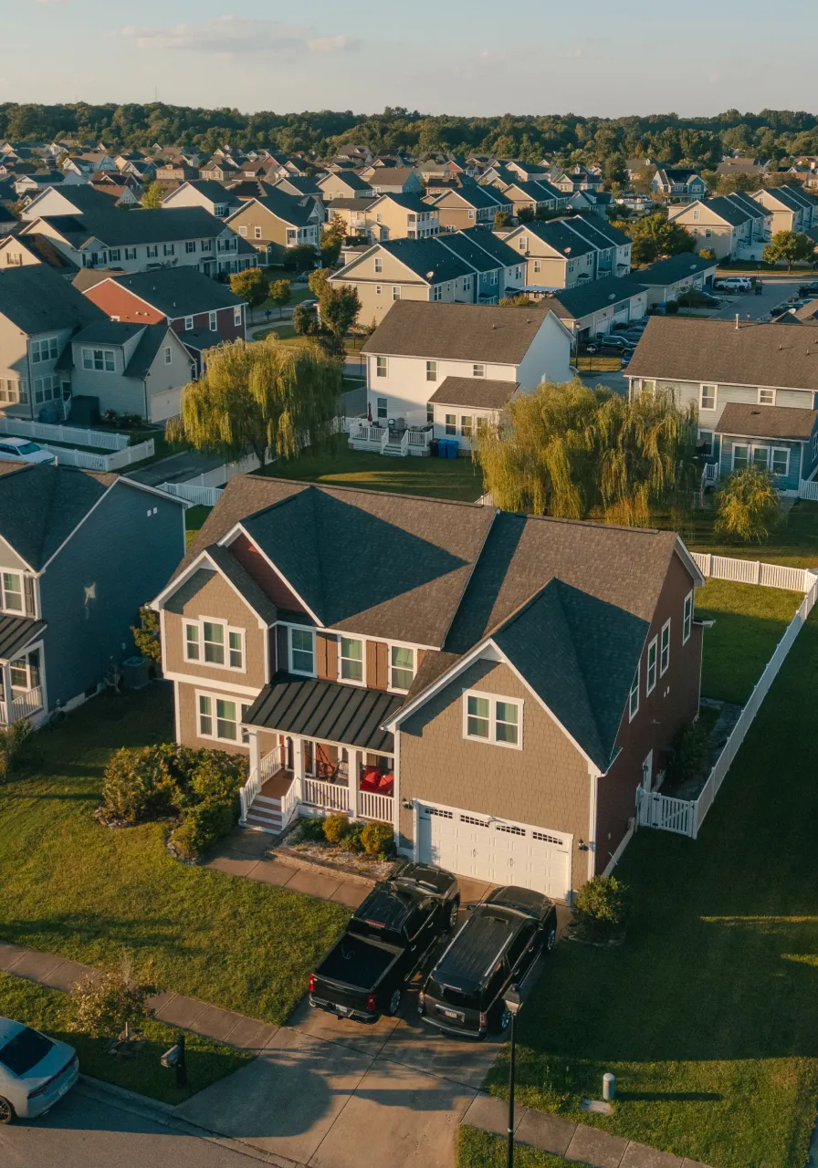 Aerial view of a suburban neighborhood with single-family houses, green lawns, and parked vehicles in driveways.