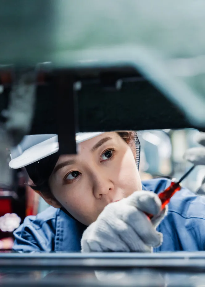 Woman wearing white gloves and a cap using a screwdriver to repair or assemble machinery.