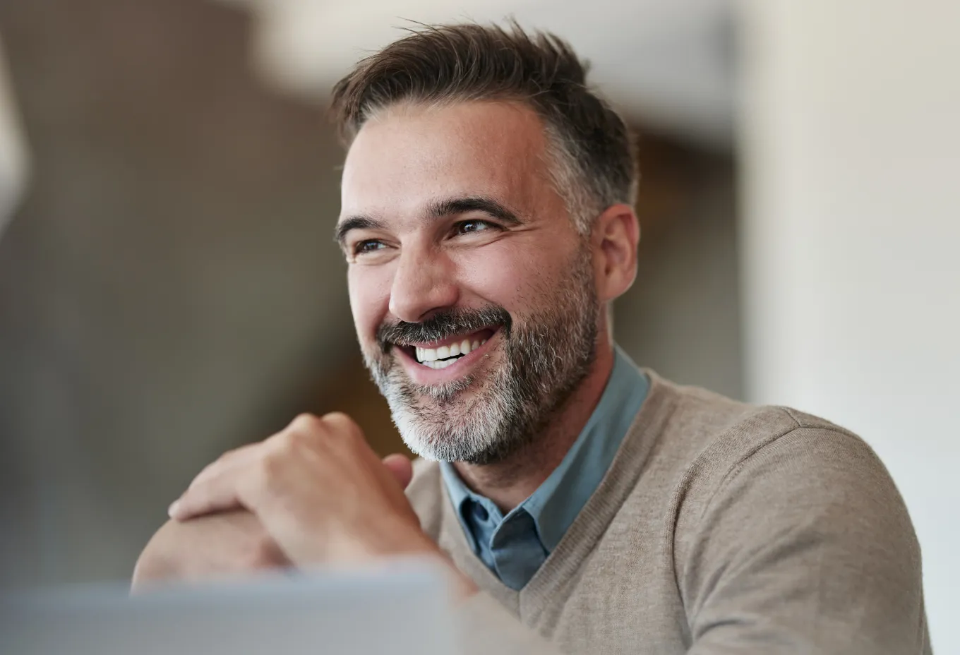 Smiling middle-aged man with gray beard resting his chin on folded hands.