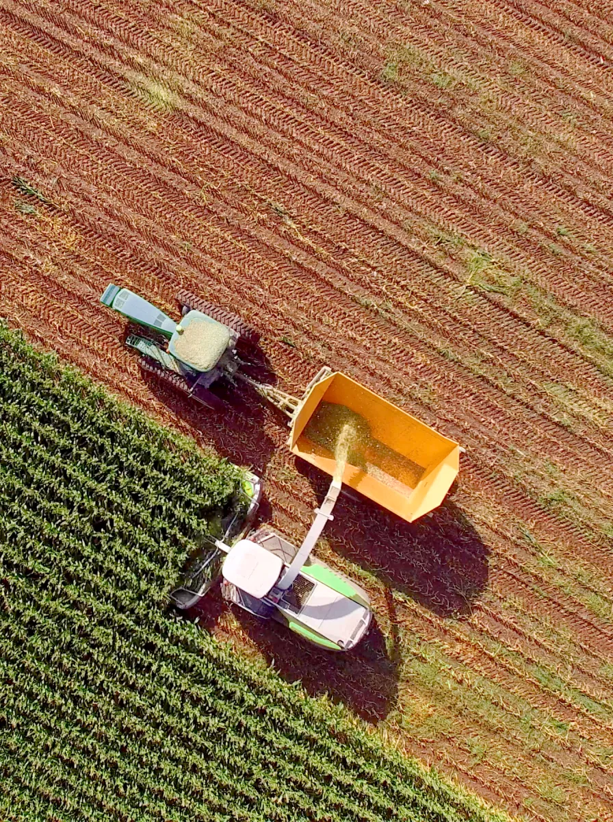 Aerial view of a combine harvester unloading harvested crops into a tractor trailer next to a green field.