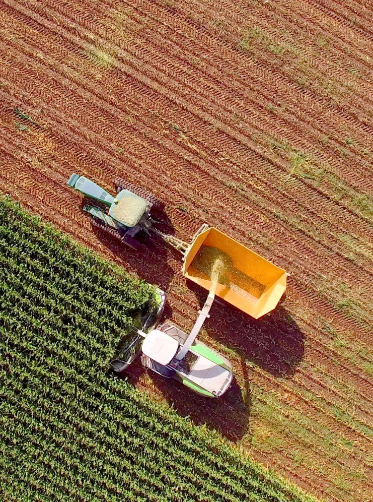 Aerial view of a combine harvester unloading harvested crops into a tractor trailer next to a green field.