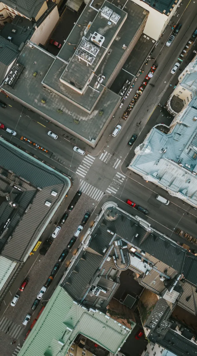 Aerial view of an urban street intersection with vehicles and surrounding buildings with varied rooftops.