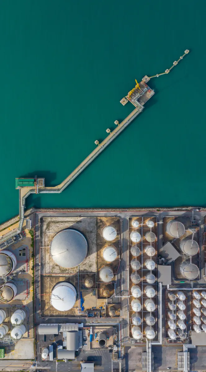 Aerial view of an industrial port with storage tanks and a long pier extending into the water.