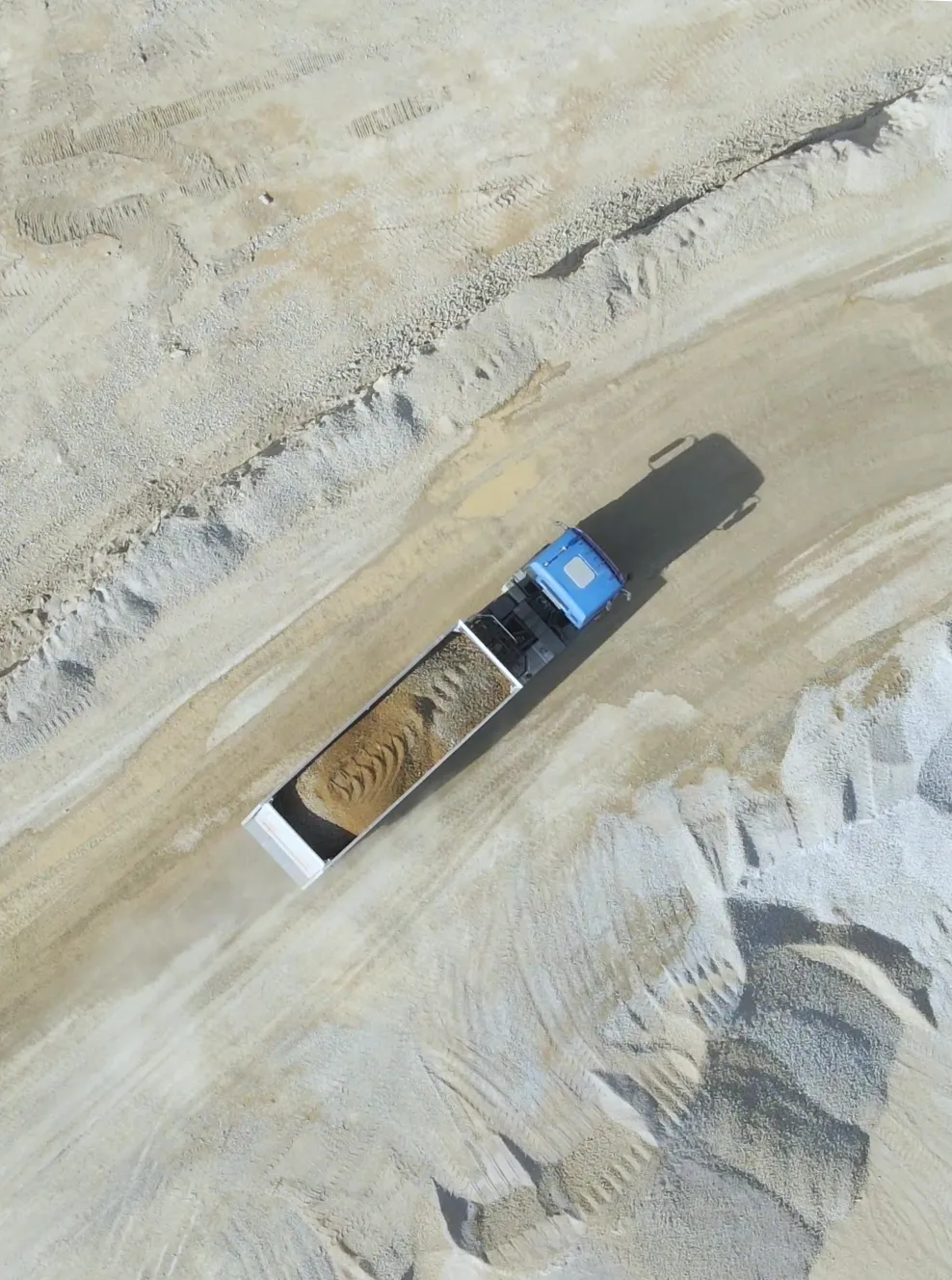 Aerial view of a blue dump truck carrying sand on a dirt road at a construction or mining site.