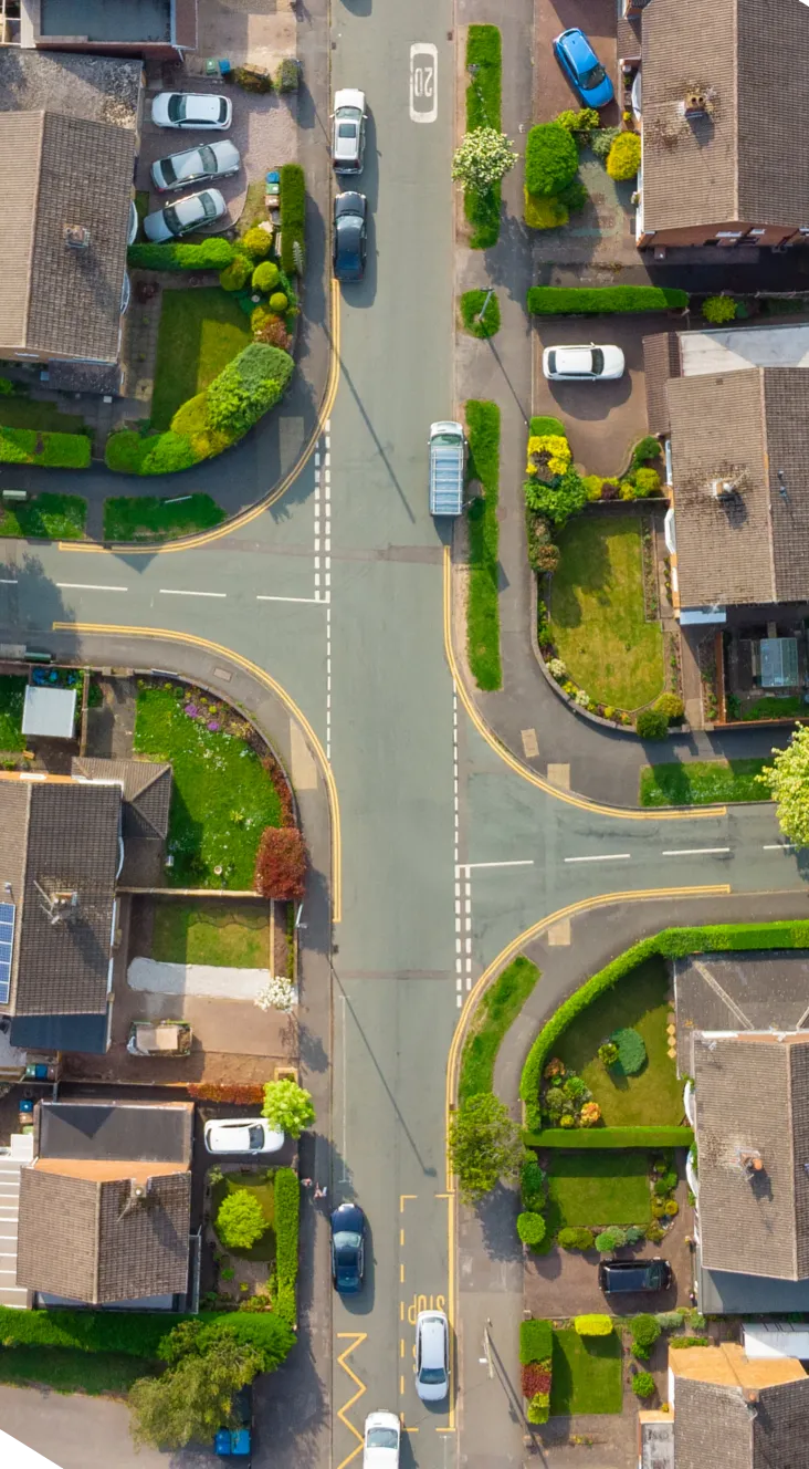 Aerial view of a residential intersection with cars, houses, green lawns, and well-maintained gardens.
