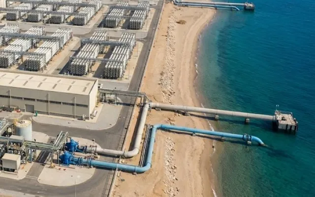 Aerial view of a coastal desalination plant with intake and outflow pipelines extending into the sea.