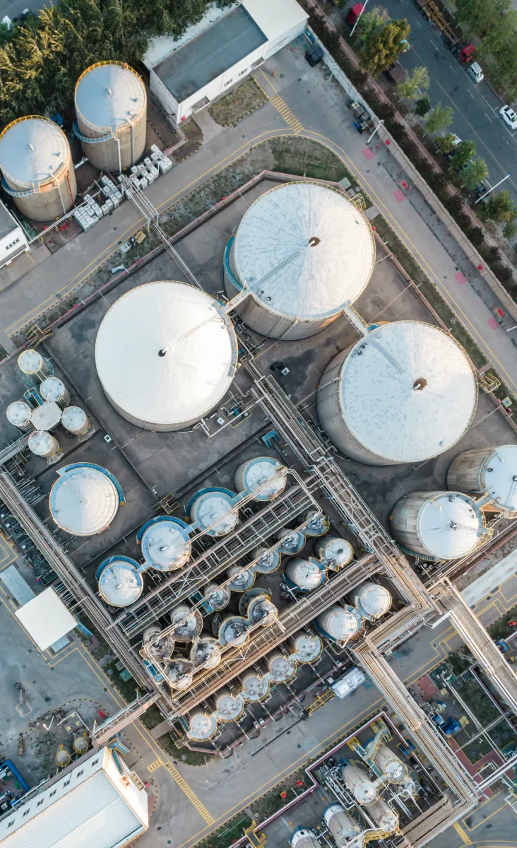 Aerial view of large industrial storage tanks and cylindrical containers connected by pipes in a refinery or chemical plant.