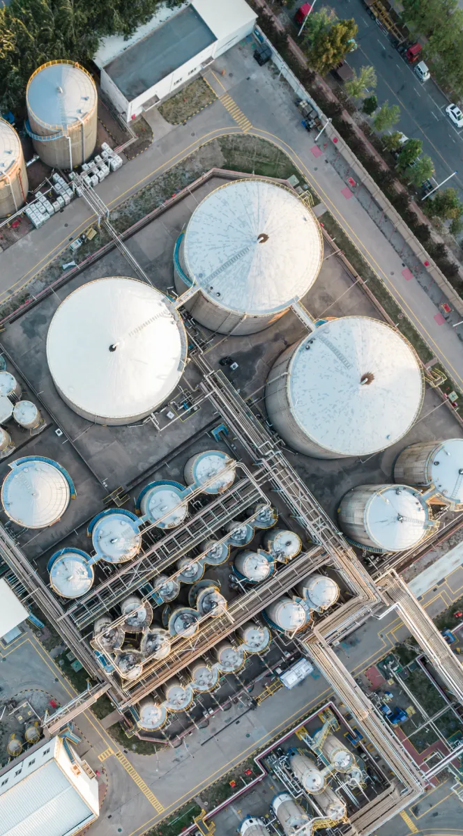 Aerial view of large industrial storage tanks and cylindrical containers connected by pipes in a refinery or chemical plant.