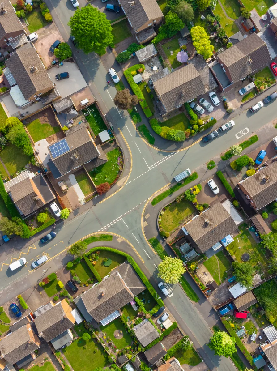 Aerial view of a residential neighborhood with an intersection surrounded by houses, gardens, and parked cars.