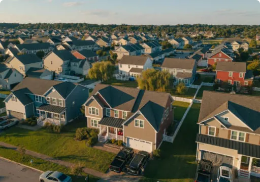 Aerial view of a suburban neighborhood with rows of houses and green lawns under a partly cloudy sky.