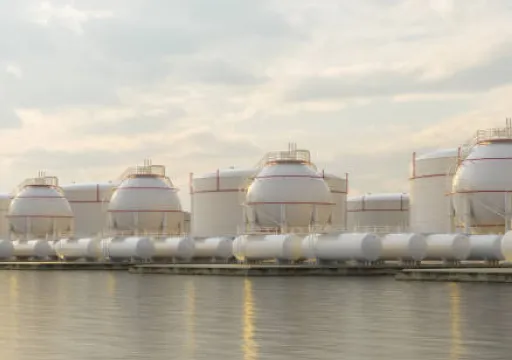 Large spherical and cylindrical industrial storage tanks near water under a cloudy sky.