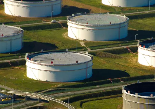 Aerial view of large white industrial storage tanks on green grass fields connected by pipelines and roads.