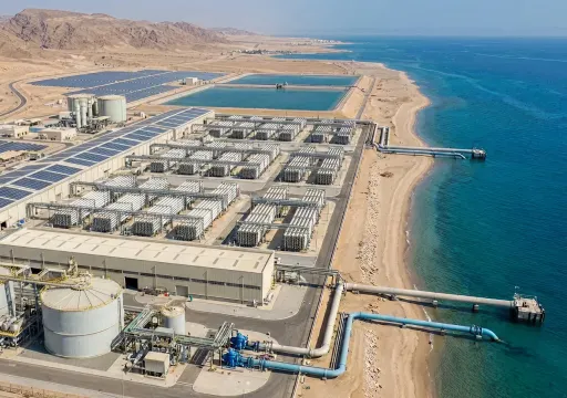 Aerial view of a coastal desalination plant with multiple rectangular processing units, large tanks, and pipelines extending into the sea.