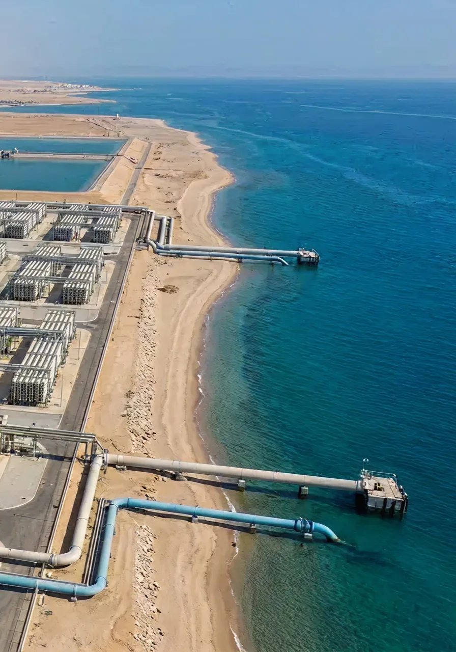 Desalination plant on a sandy coastline with large pipes extending into the blue ocean water.