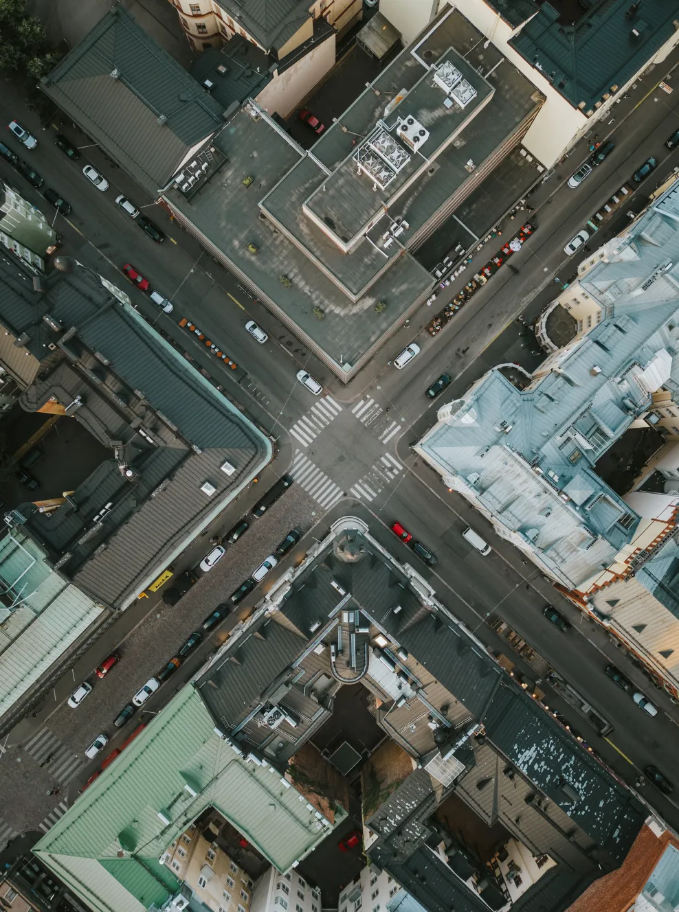 Aerial view of an urban intersection with crosswalks, surrounded by tall buildings with varied rooftops and parked cars along the streets.