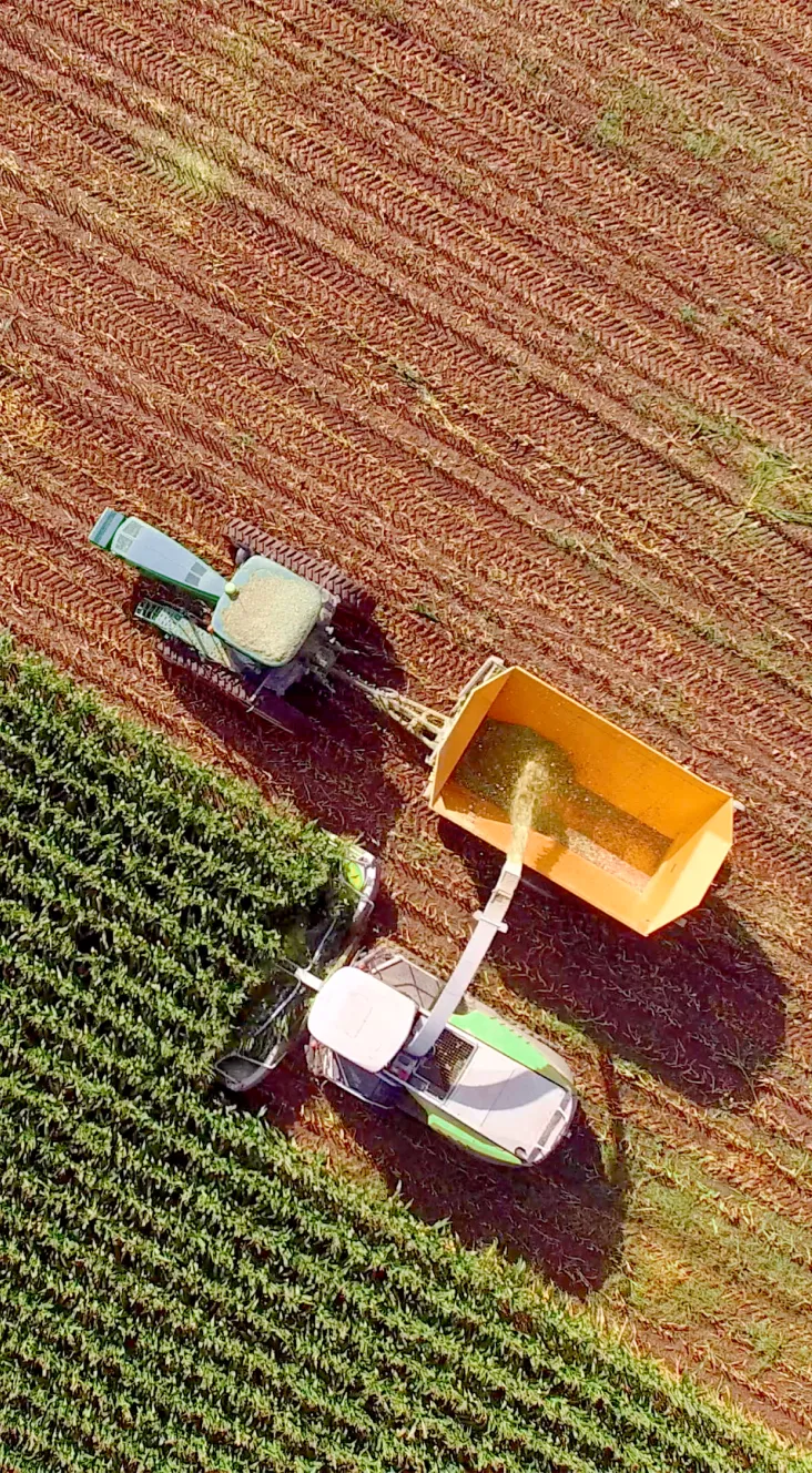 Aerial view of a combine harvester unloading harvested crops into a tractor trailer next to a green field.