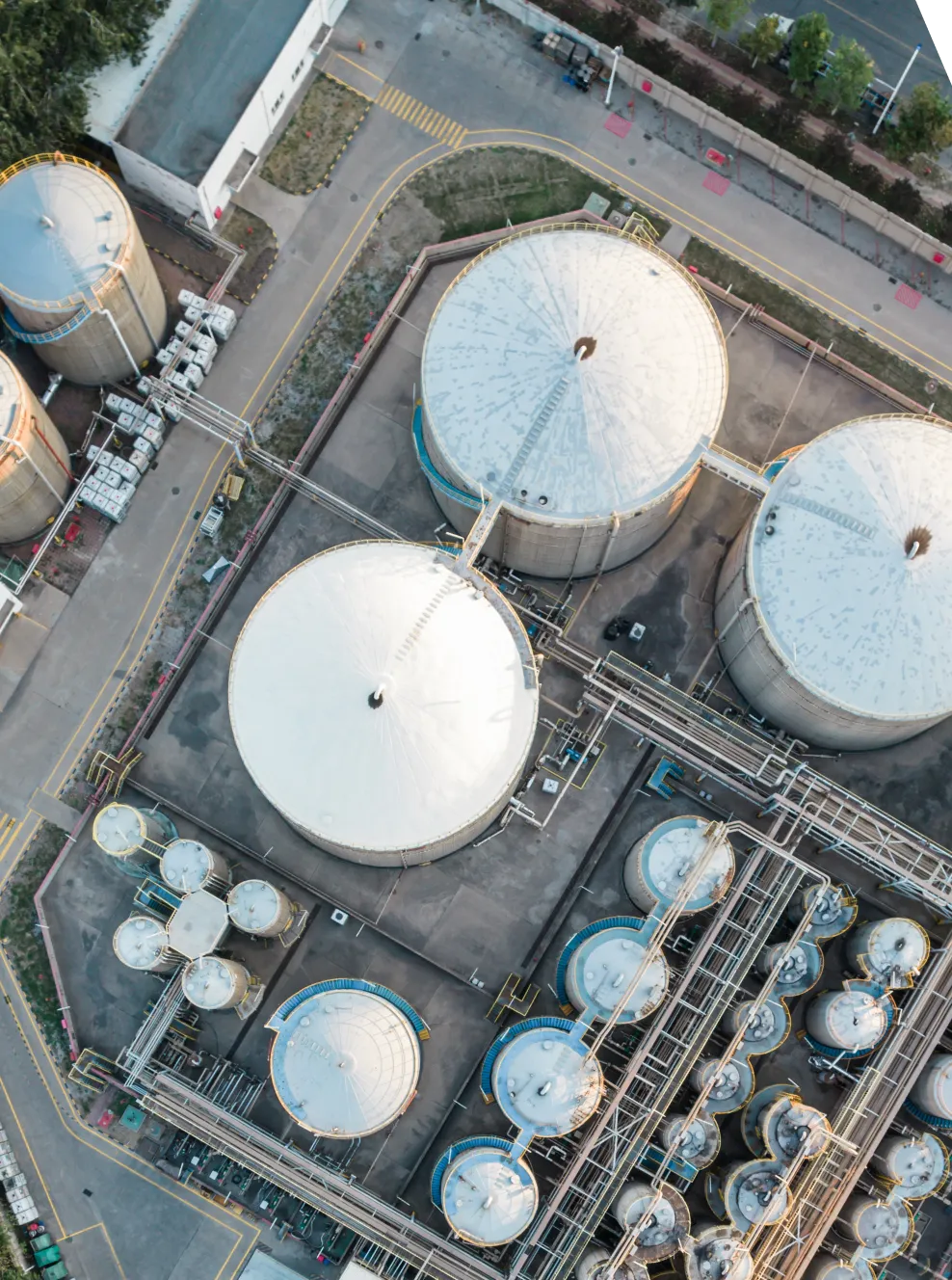 Aerial view of large industrial storage tanks and cylindrical containers connected by pipes in a refinery or chemical plant.