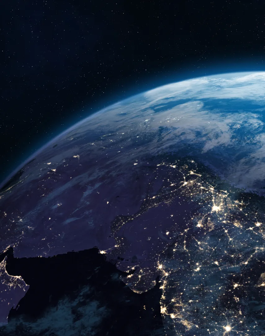 Nighttime satellite view of Earth showing illuminated cities and landmasses under a starry sky.