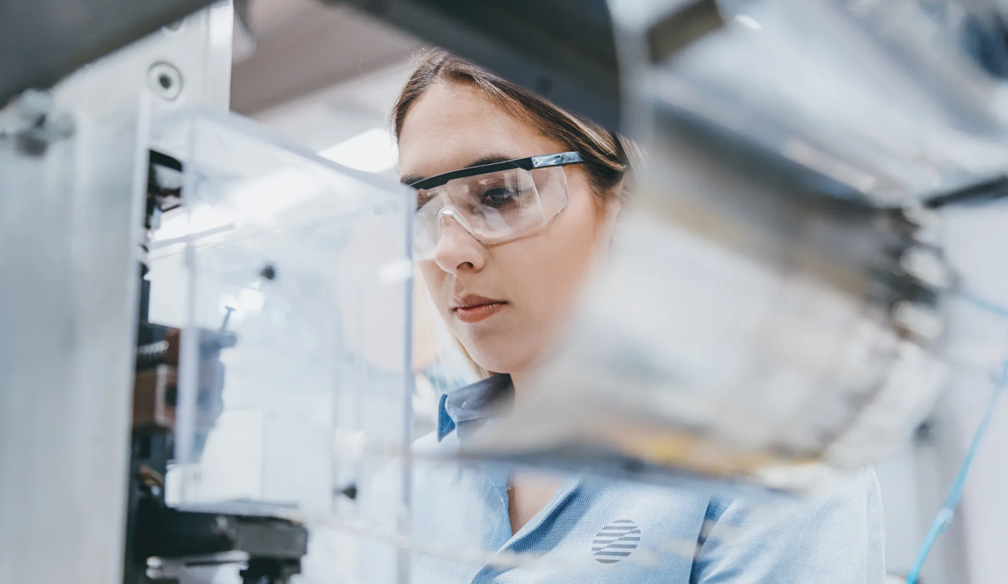 Woman wearing safety glasses closely inspecting industrial machinery.