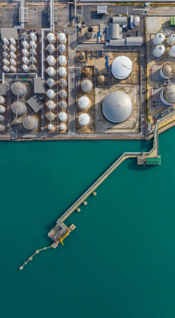 Aerial view of an industrial port with storage tanks and a long pier extending into the water.