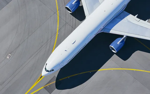 Aerial view of a white commercial airplane with blue engines parked on an airport tarmac with yellow taxiway lines.
