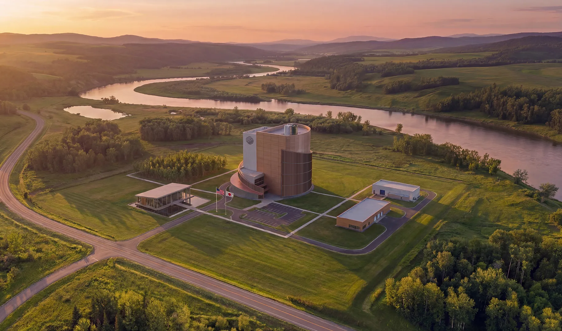 ZettaJoule modern building complex with surrounding smaller buildings near a winding river at sunset in a green rural landscape.