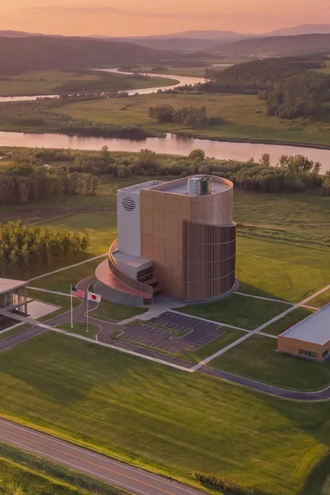 ZettaJoule modern building complex with surrounding smaller buildings near a winding river at sunset in a green rural landscape.