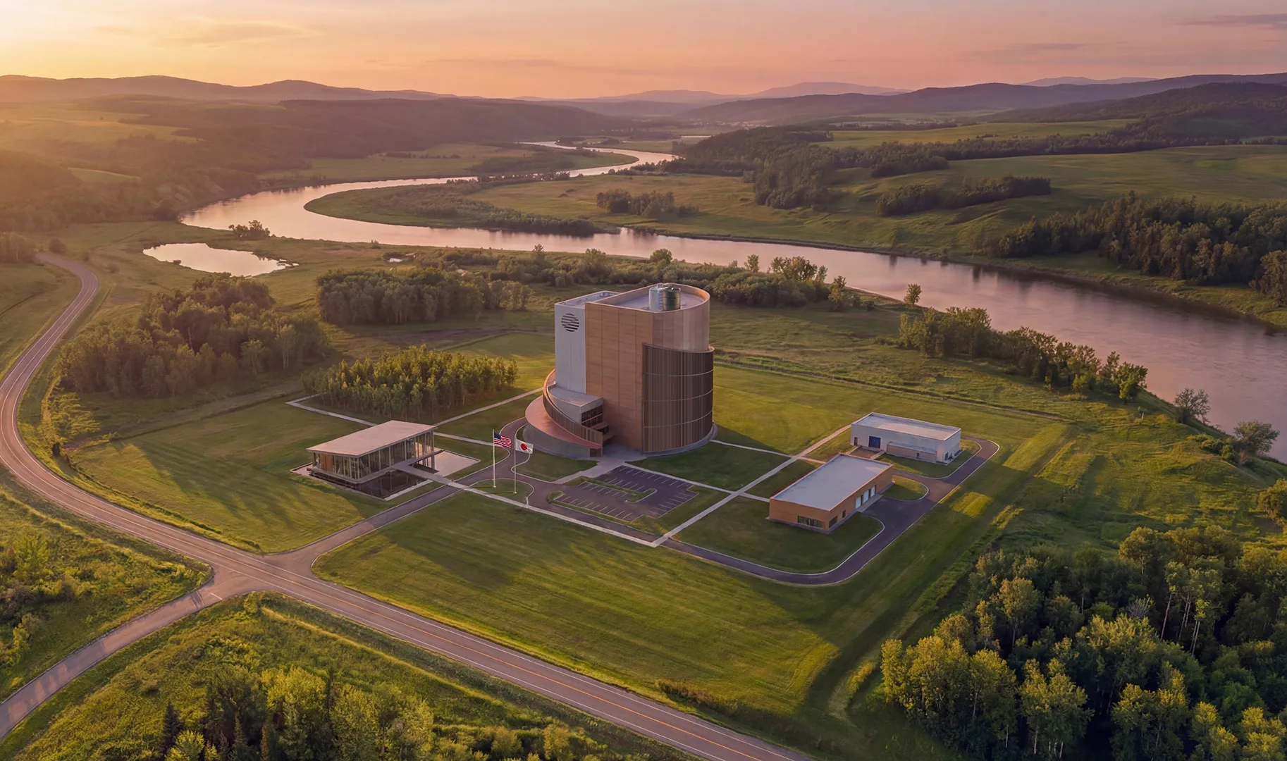 ZettaJoule modern building complex with surrounding smaller buildings near a winding river at sunset in a green rural landscape.