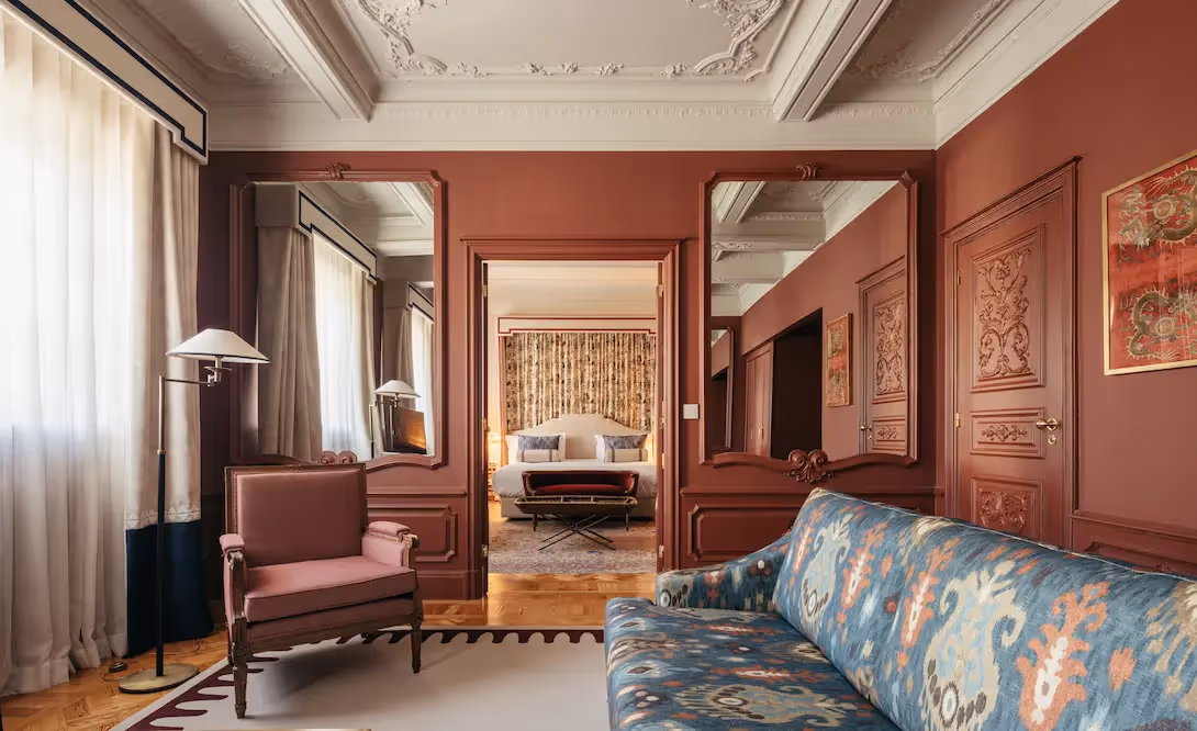 Living area toward the bedroom at Hotel Experimental Infante Sagres in Porto, featuring a pink armchair and blue patterned sofa.